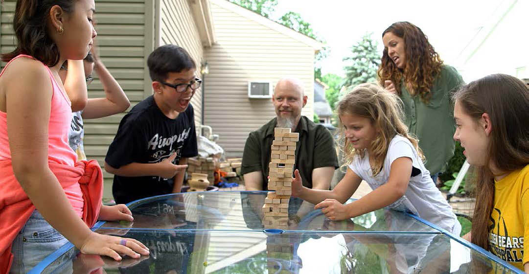 A group of children and adults sitting and standing around a table playing Jenga.