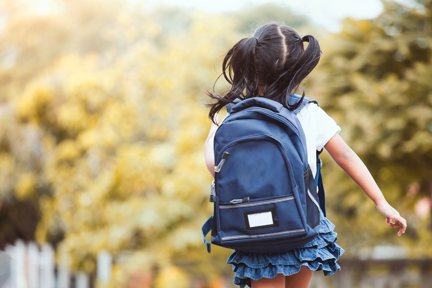 Girl with pigtails running towards school with a backpack on.