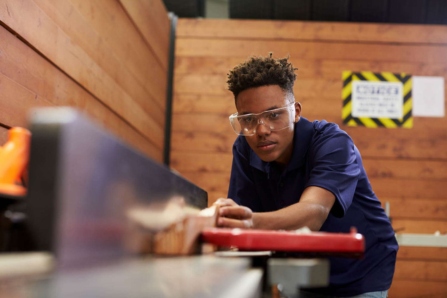 Transition-age student wearing safety goggles and working with wood and machinery.