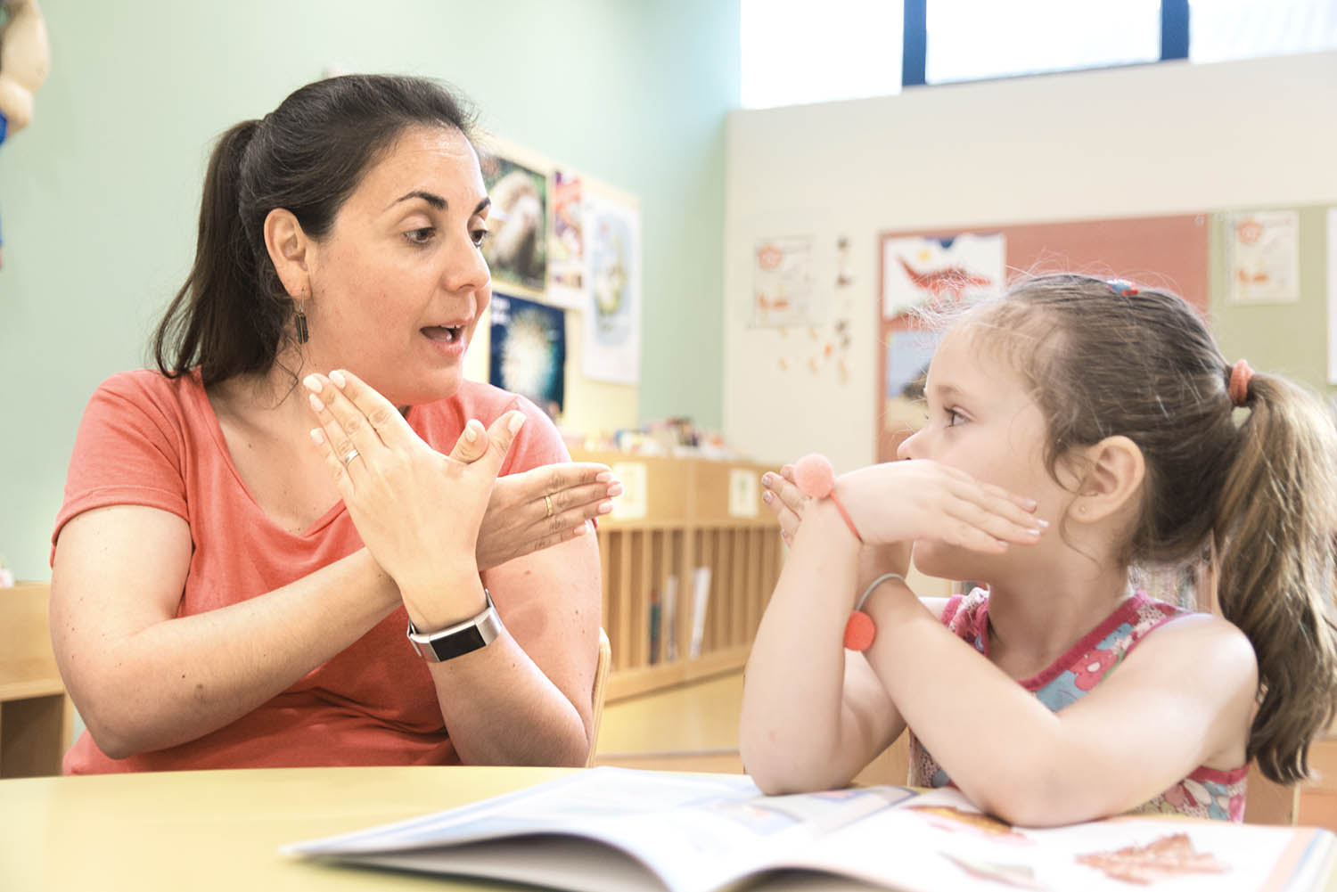 Student and teacher sitting at a table reading a book and signing 'butterfly'