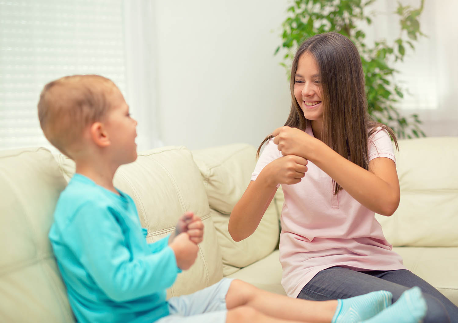 Two children sitting on the couch together, both signing 'make'.