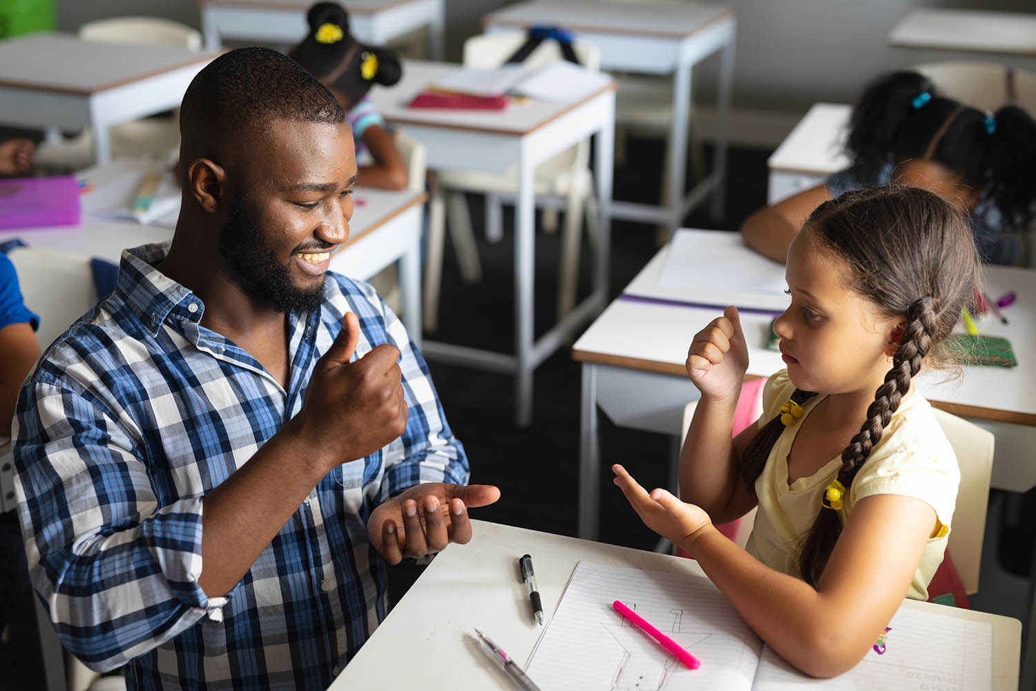 Student and teacher in a classroom, both signing ‘help’.