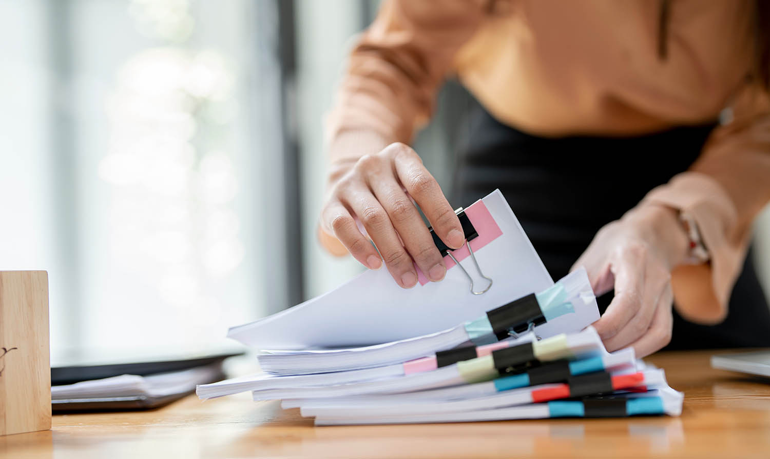 A pile of paperwork organized with binder clips with a person's hands flipping through it.