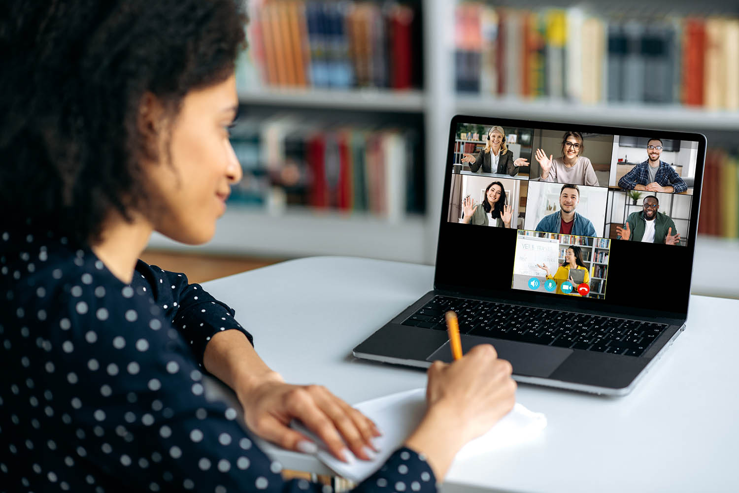 An adult taking notes while sitting at a computer in a virtual meeting.