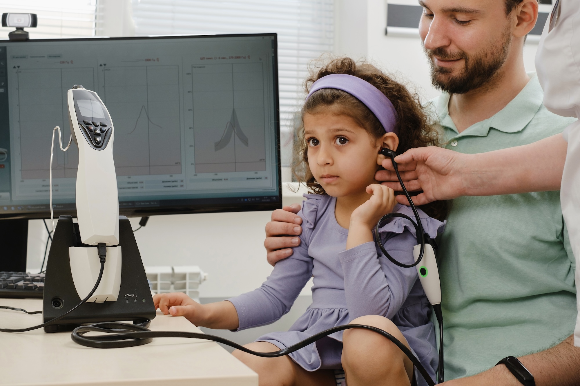 Young girl sitting on an adult’s lap getting her hearing checked