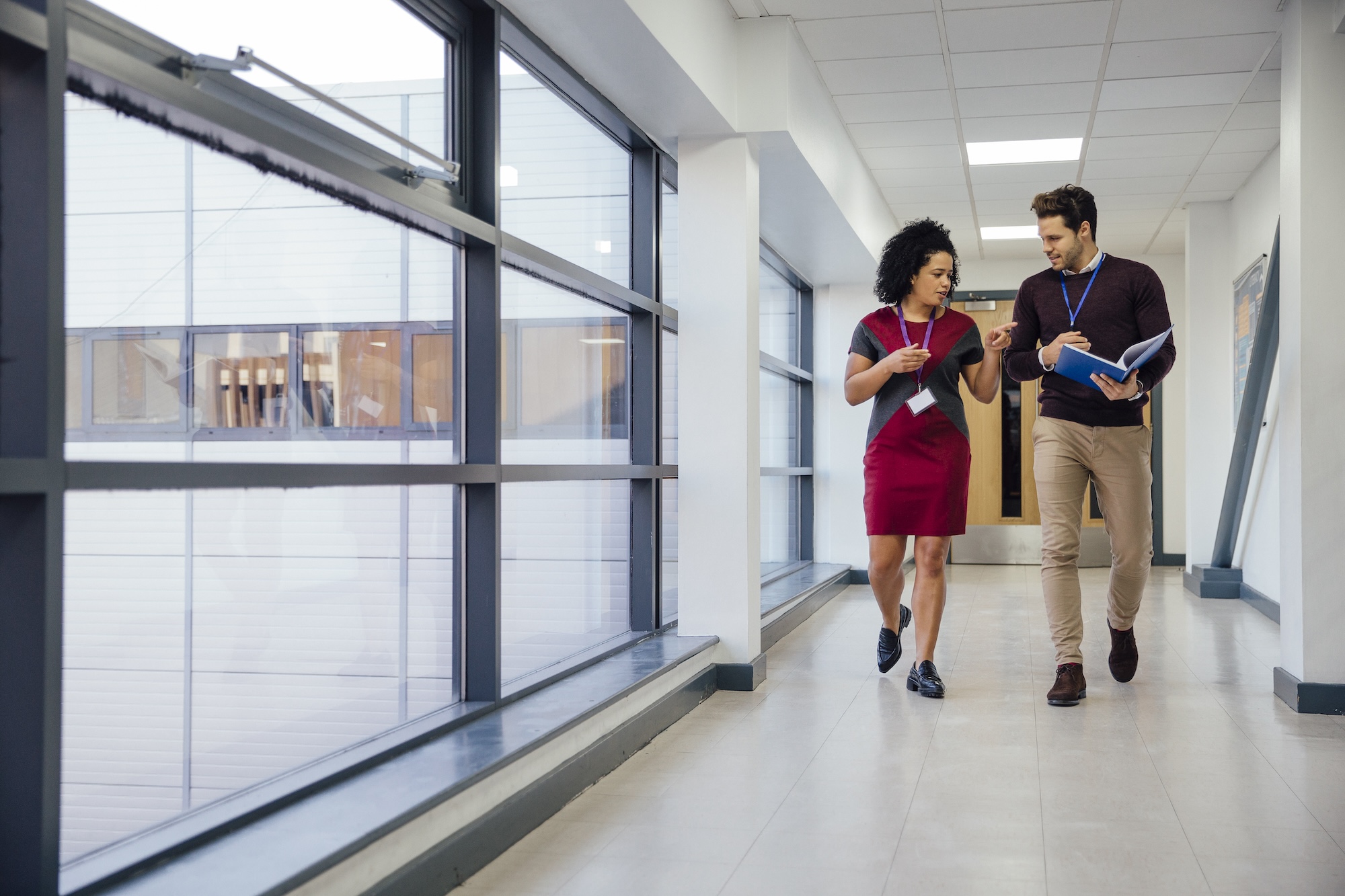 Two adults walking through a school hallway discussing information in a binder