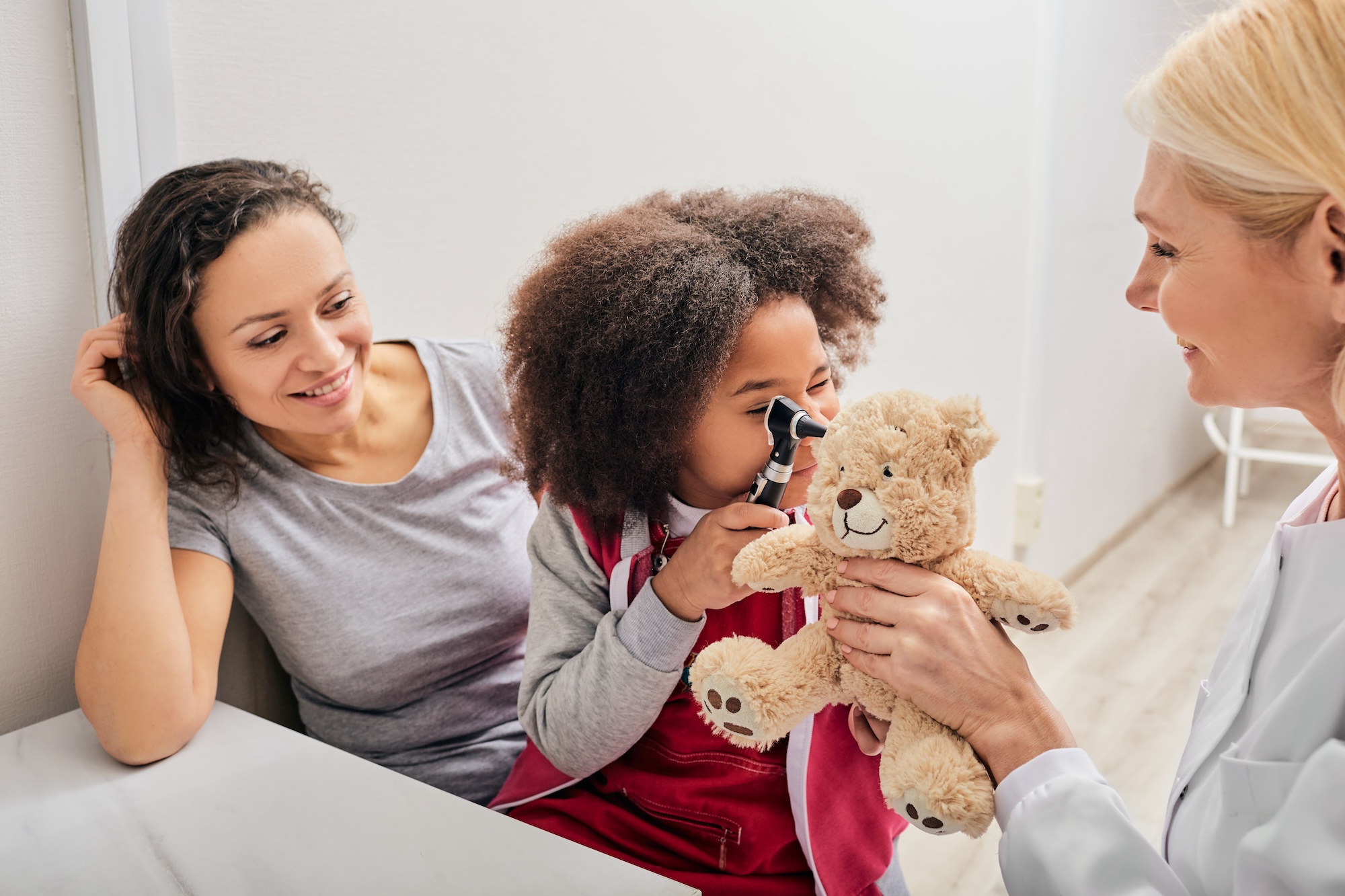 Young girl using an otoscope on a teddy bear at the doctor’s office