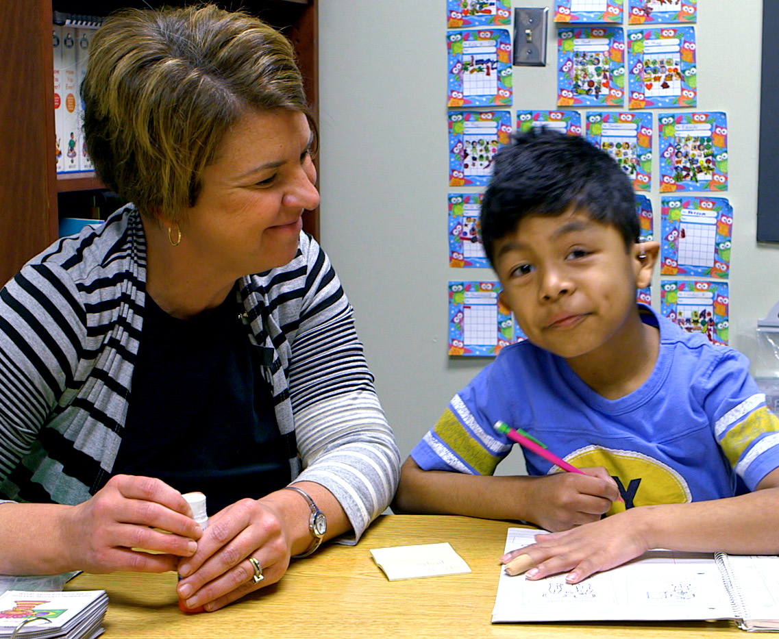 Teacher and student with hearing aid sitting side by side at a table