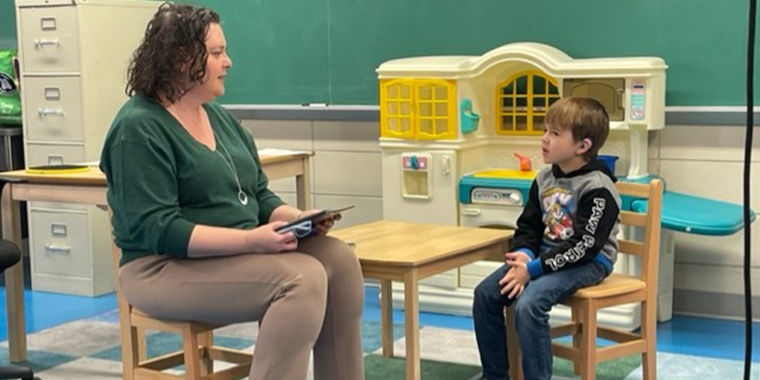 Student and audiologist facing each other, sitting at a small table during the administration of the Functional Listening Evaluation